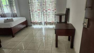 Quarto de hotel com uma cama, uma pequena mesa de madeira e uma janela com cortinas.