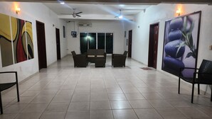 A spacious hallway with tiled flooring, a central seating area with a sofa and chairs, ceiling fans, and wall-mounted artwork.