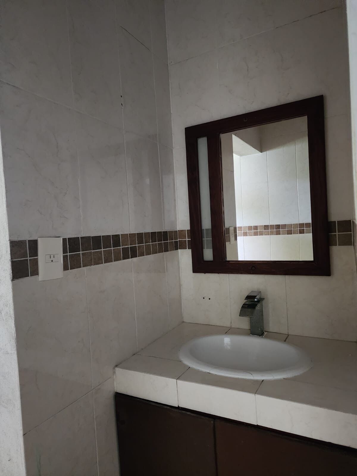 A bathroom with a white sink, a mirror with a wooden frame, and a tiled backsplash.