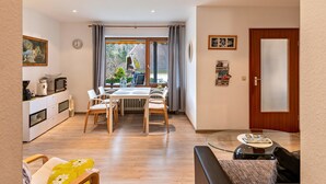 Un soggiorno moderno con zona pranzo, cucina e un'ampia finestra con tende.