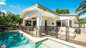 Una casa moderna con piscina, porche cubierto y zona de estar al aire libre.