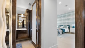 Habitación de hotel moderna con una cama grande, un baño con espejo y un pasillo que conduce a otra habitación.