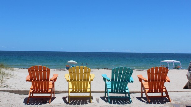 Cuatro sillas Adirondack sobre una playa arenosa con vista despejada al océano.
