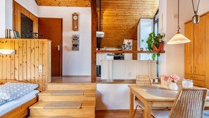 Un interior de madera con una cama, una mesa de comedor con sillas, una zona de cocina y un techo de madera.