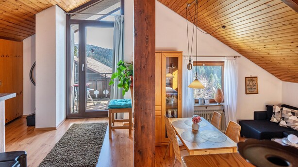 Una habitación amplia con techo de madera, un comedor con mesa y sillas, un sofá y un ventanal con vistas al exterior.