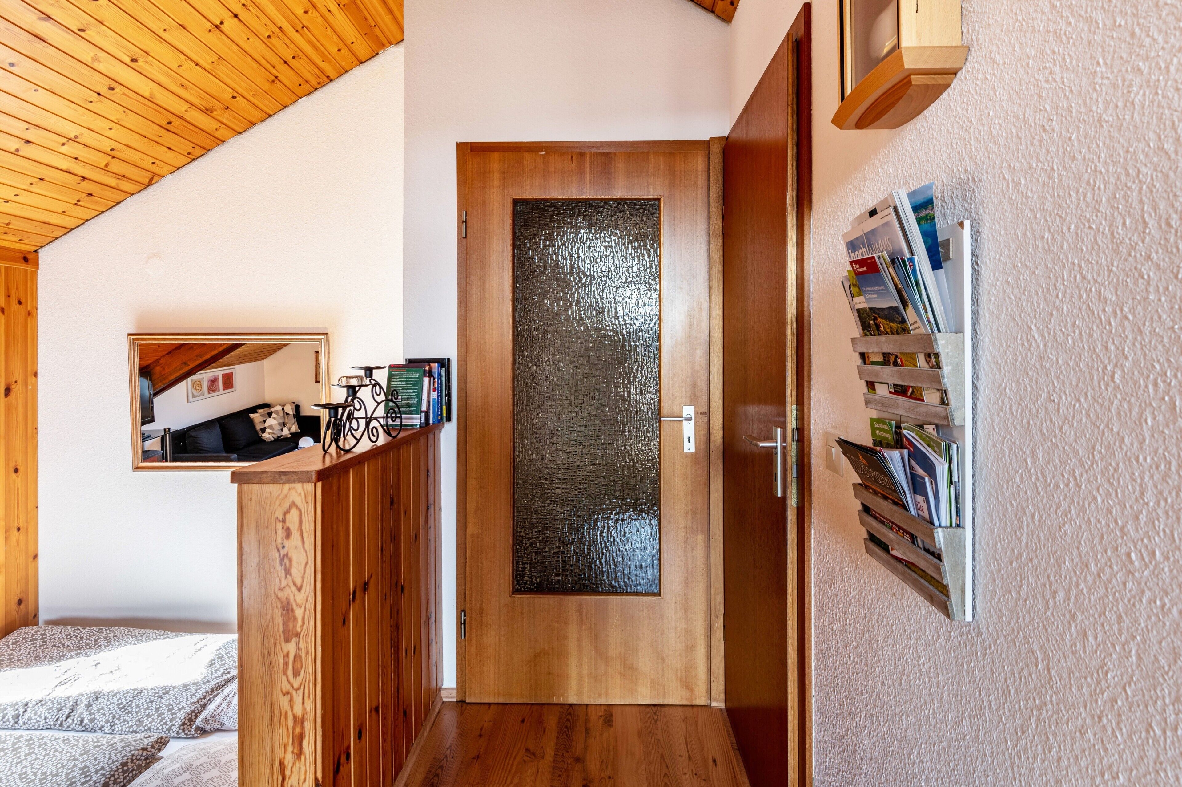 Interior de fusta amb una porta de vidre, una biblioteca i un mirall que reflecteix una habitació amb un llit.