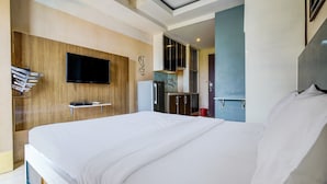 A modern hotel room with a large bed, a flat-screen TV mounted on the wall, a small kitchenette, and a bathroom visible through an open door. - OYO Life 93251 Apartement Gateway Cicadas By Alugada (Bandung)