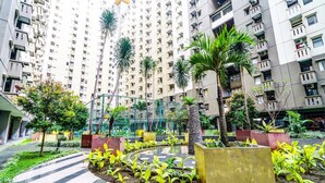A residential building with multiple floors, balconies, and a landscaped courtyard with palm trees and plants. - OYO Life 93251 Apartement Gateway Cicadas By Alugada (Bandung)