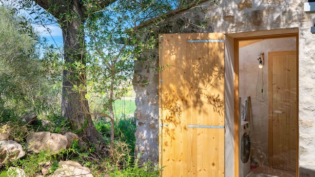 Une porte en bois rustique qui donne sur un petit espace clos, avec un mur en pierre et une vue sur l’extérieur.