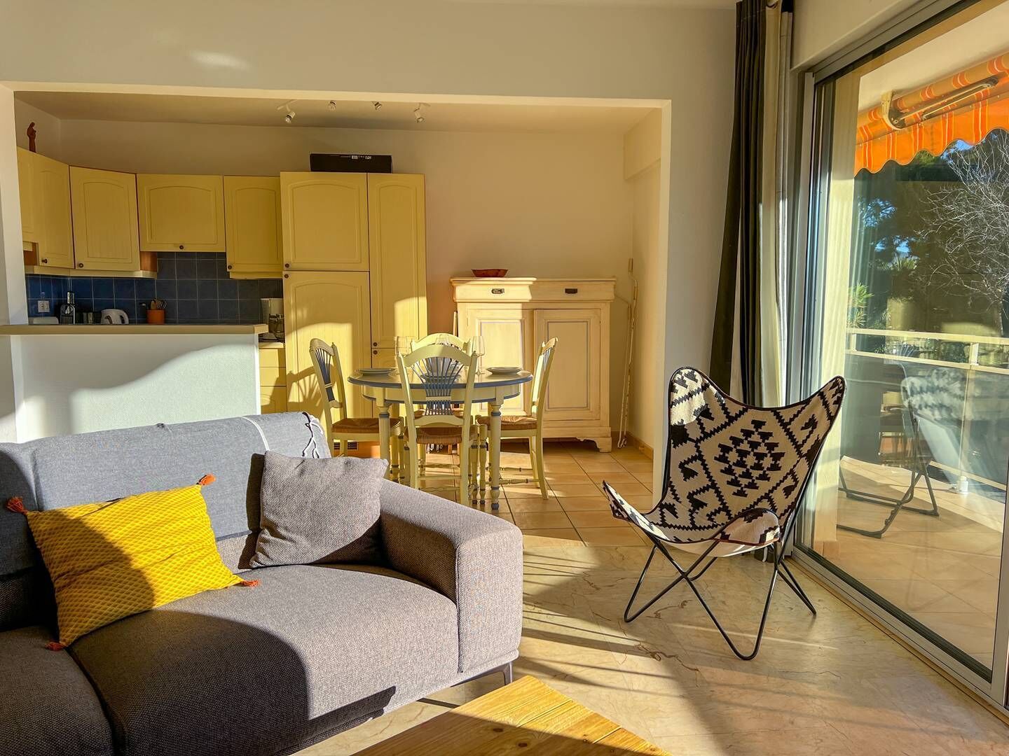 Un salon moderne avec un canapé gris, un fauteuil à motifs et un coin repas comprenant une table ronde et des chaises.
