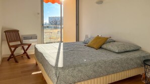 Een slaapkamer met een bed, een stoel, een tafel en uitzicht door een deur.