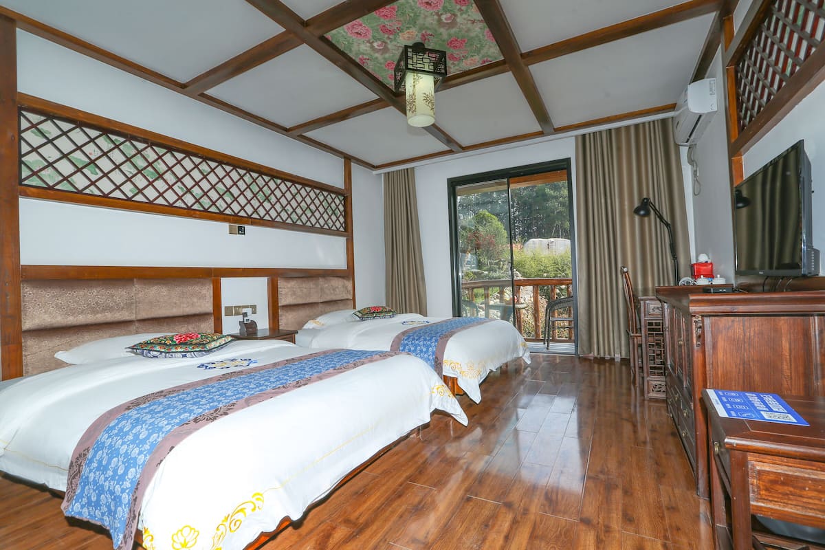 A hotel room with two beds, a wooden floor, a traditional ceiling design, and a view of the outdoors.