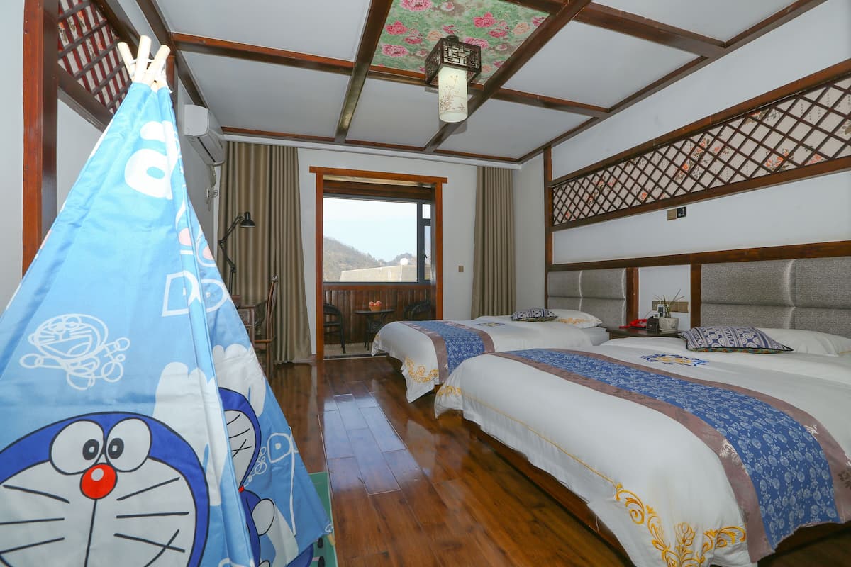 A hotel room with two beds, a wooden floor, a view through a door, and a hanging blue curtain with cartoon characters.