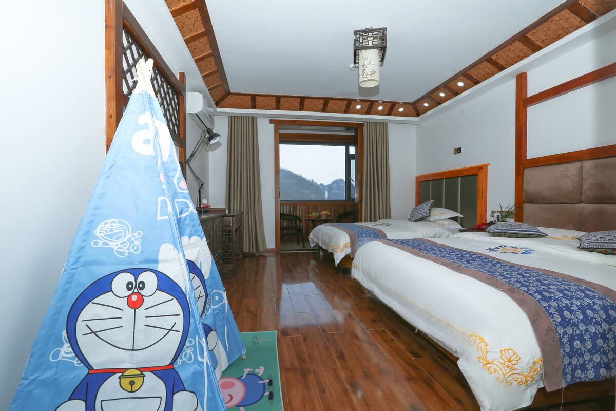 A hotel room with two beds, a large window, and a view of mountains.
