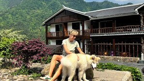A person sitting on a stone patio with a large dog in front of a traditional wooden building with a balcony. - mountainside (Zhangjiajie)