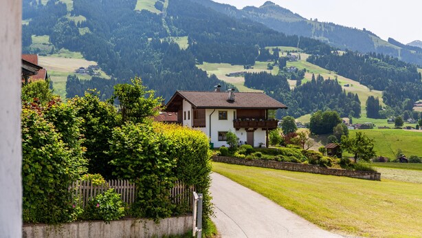 A rural house with a garden, a paved path, and a mountain backdrop. - 'Feichtenhäusl 1' with Mountain View, Private Terrace and Wi-Fi (Westendorf)