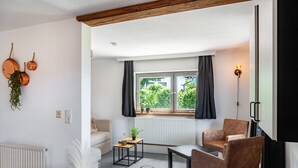 A modern living room with a sofa, two armchairs, a coffee table, and a dining table. There is a window with curtains, a radiator, and a wall-mounted light fixture. - 'Feichtenhäusl 1' with Mountain View, Private Terrace and Wi-Fi (Westendorf)