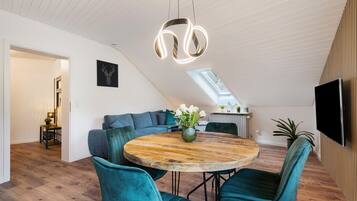 Un loft moderno con comedor que incluye una mesa redonda de madera y sillas color turquesa, una sala de estar con sofá y un tragaluz.
