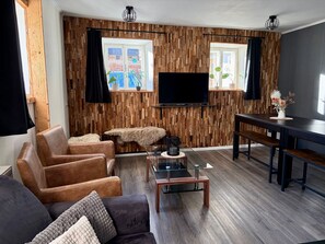 Un salon moderne avec un mur recouvert de panneaux en bois, des canapés en cuir, une table basse en verre et un téléviseur à écran plat.