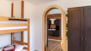 Een stapelbed, een houten garderobe en een keuken met kastjes en een plant.