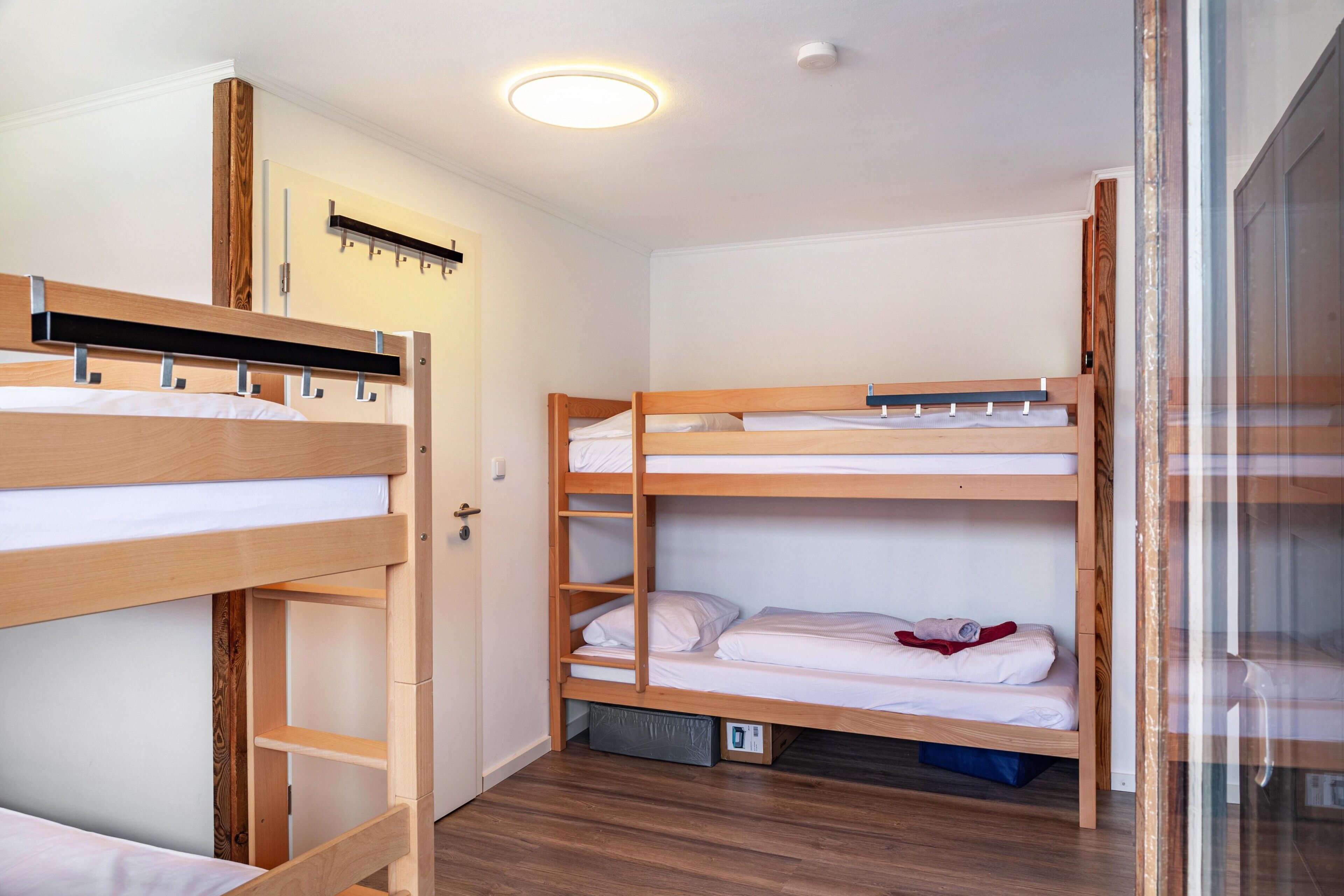 Une chambre avec des lits superposés, une armoire en bois et un luminaire au plafond.
