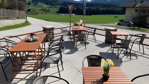 Een terras met tafels en stoelen, een straatnaambord en uitzicht op een berg.
