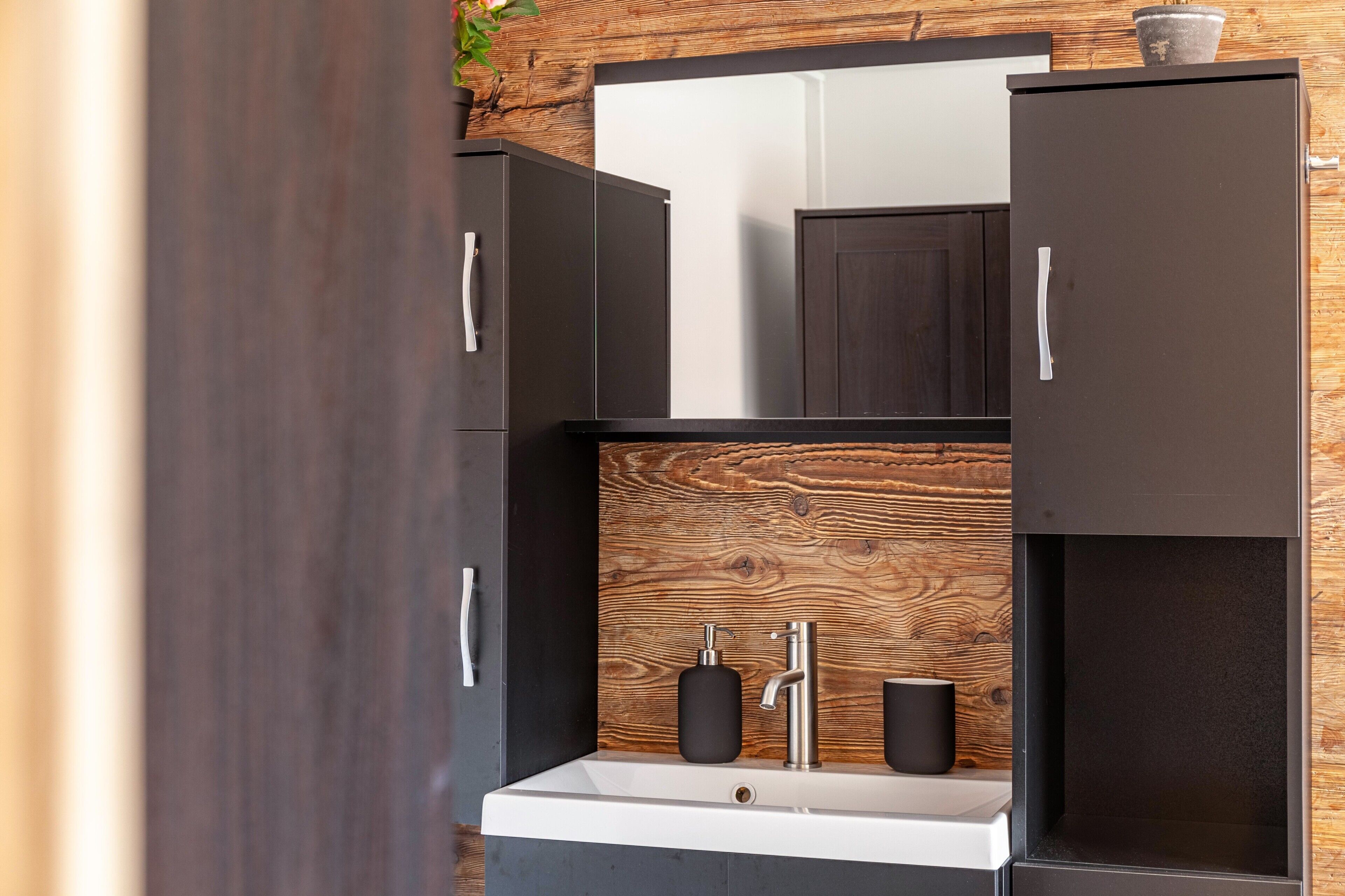 Een moderne badkamer met een houten wand, een witte wasbak en donkere kasten.