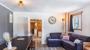 Een moderne woonkamer met een donker houten vloer, een donkere bank, een glazen salontafel, een wandklok en een houten deur die naar een keuken leidt.