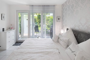 Quarto com cama, penteadeira, cadeira e vista para o exterior.