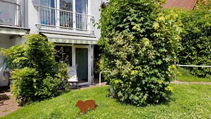 Ein Wohngebäude mit Balkon, einer Tür und einem Garten mit Hecke und Rasen.