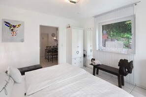 Quarto com cama, um banco, um guarda-roupa e janela com vista para o verde.