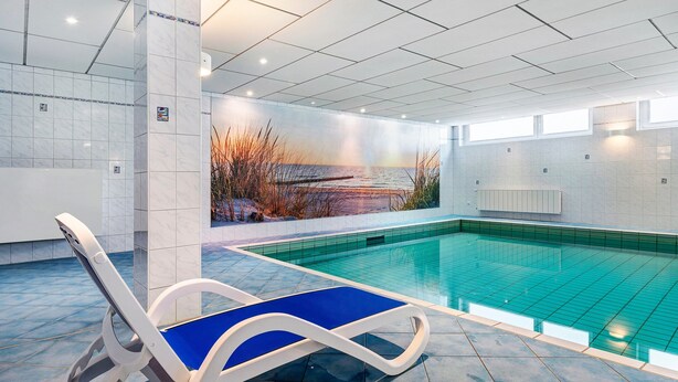 An indoor swimming pool with a mural, a lounge chair, and tiled walls.