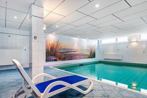 An indoor swimming pool with a mural, a lounge chair, and tiled walls. - Apartment 'Wellness Strandperle' with Garden, Private Balcony and Wi-Fi (Cuxhaven)