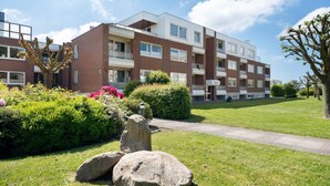 A multi-story residential building with a brick facade, balconies, and a well-maintained lawn with rocks and flowers.