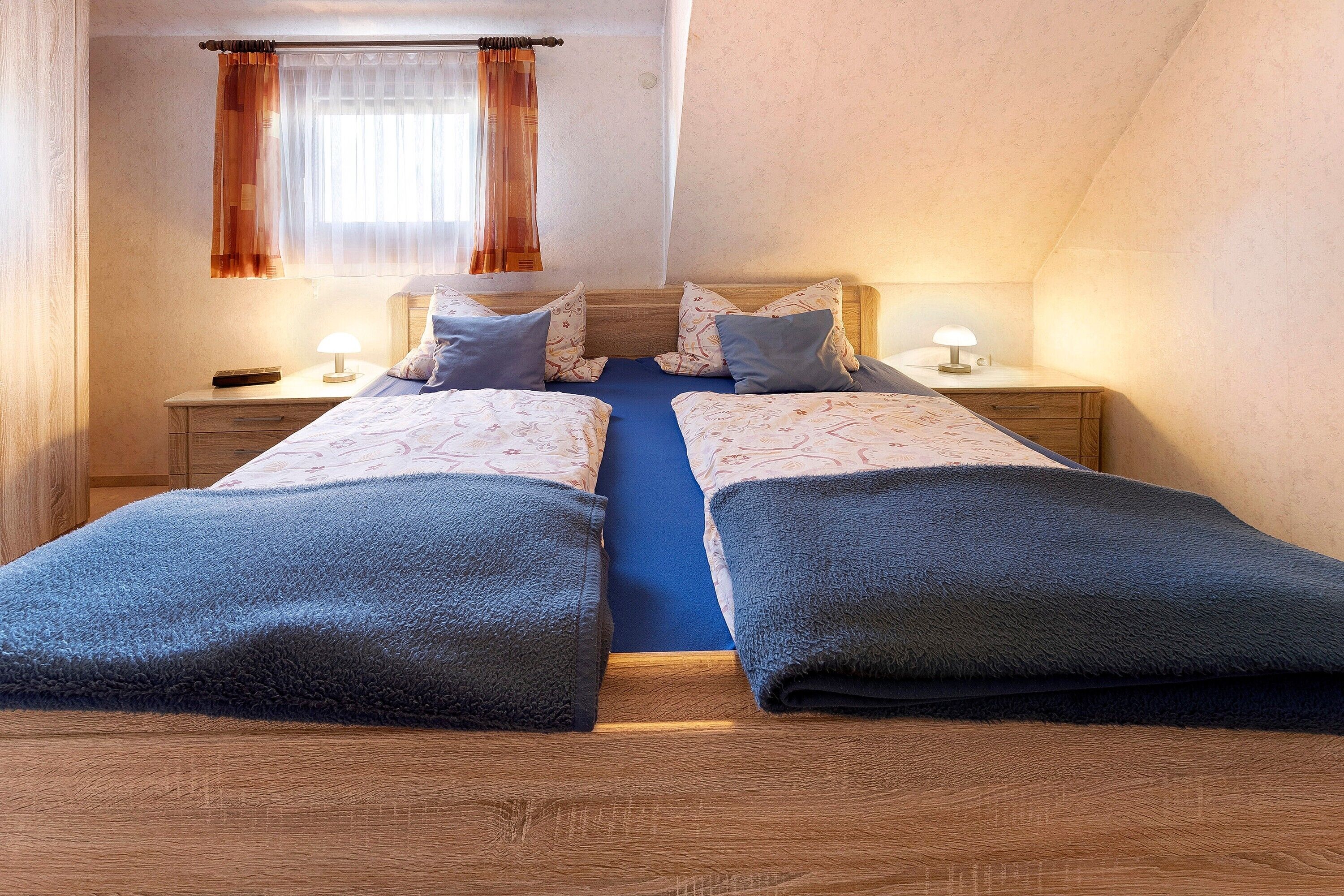 A twin room with two beds, a nightstand with a lamp, and a window with curtains.