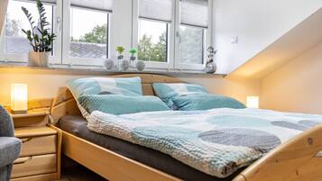 Een slaapkamer met een houten bed, nachtkastje, stoel en een raam met jaloezieën.