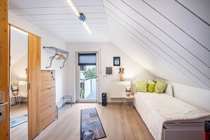 Un dormitorio con cama, un radiador, una ventana, una puerta y un pasillo.