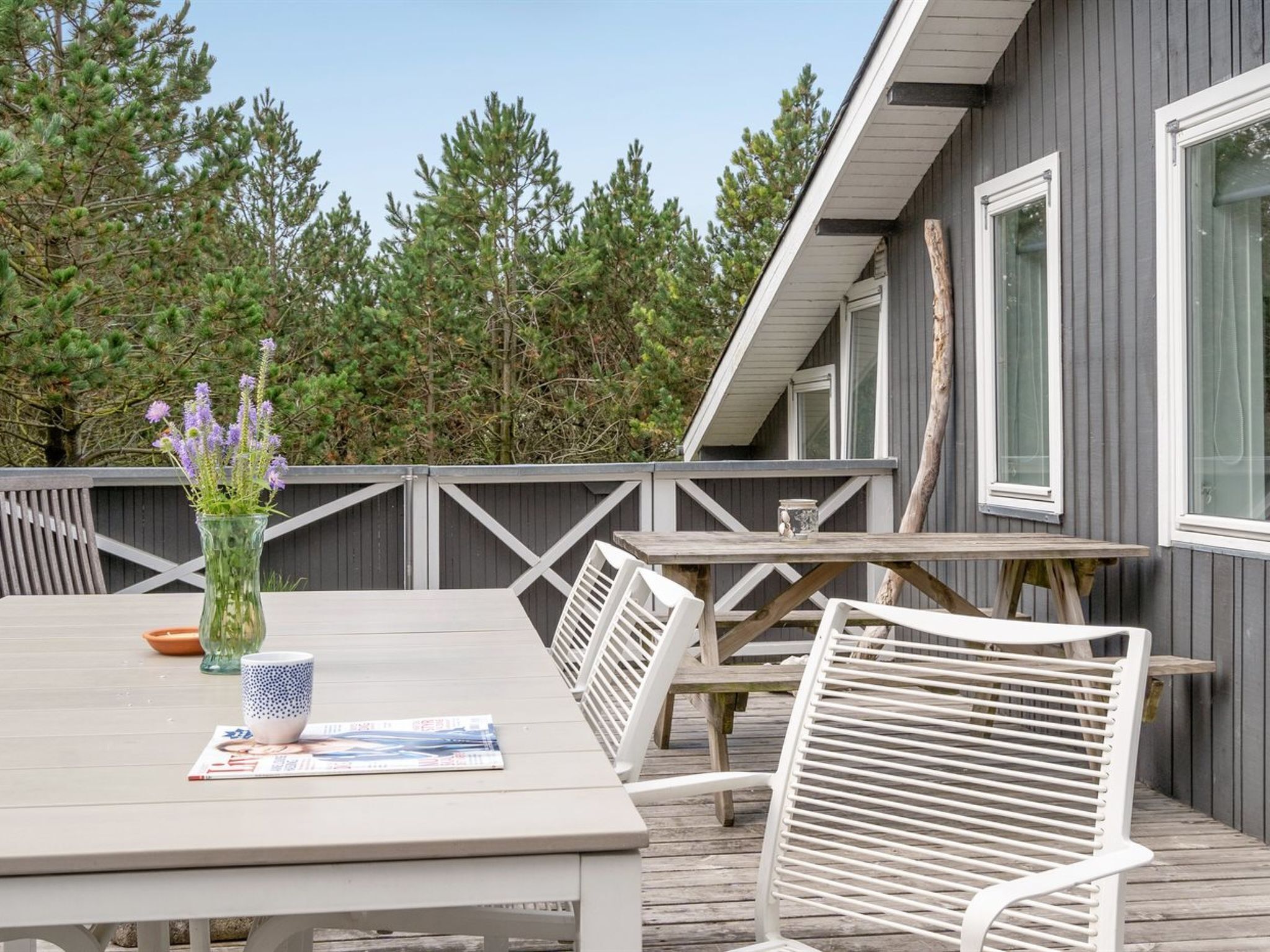 A wooden deck with a table and chairs, a vase with flowers, and a magazine.