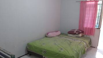 A small, simple room with a single bed, a bench, and a window with a pink curtain.