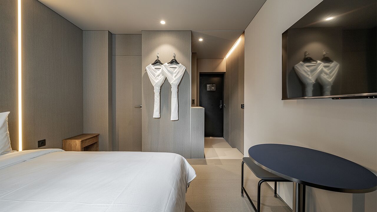 A modern hotel room with a bed, a small table, a mirror, and a wall-mounted towel rack.