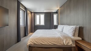 Une chambre d’hôtel moderne avec un grand lit, une table de chevet en bois et deux fenêtres avec des rideaux.