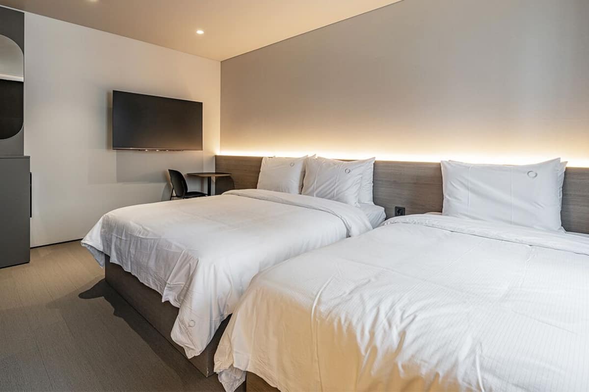 Una habitación de hotel moderna con dos camas, un televisor de pantalla plana montado en la pared, una pequeña mesa y una zona de estar.