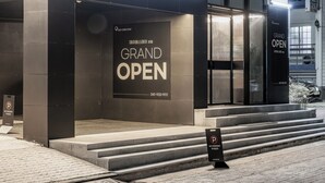 L’entrée d’un hôtel, avec une pancarte indiquant « Grande ouverture », des marches menant à la porte et un panneau « Stationnement interdit » sur le trottoir.