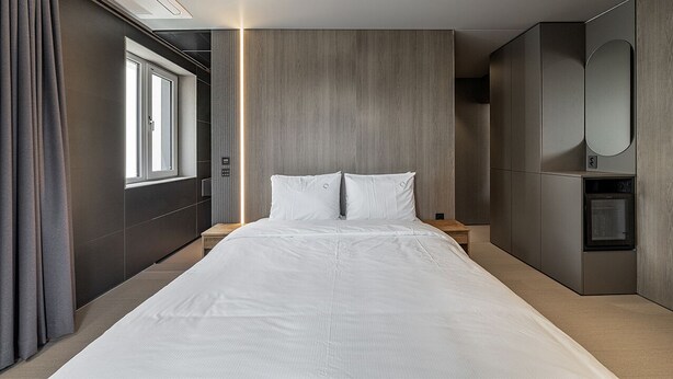 Une chambre d’hôtel moderne avec un grand lit, une table de chevet, une armoire et une fenêtre avec des rideaux.