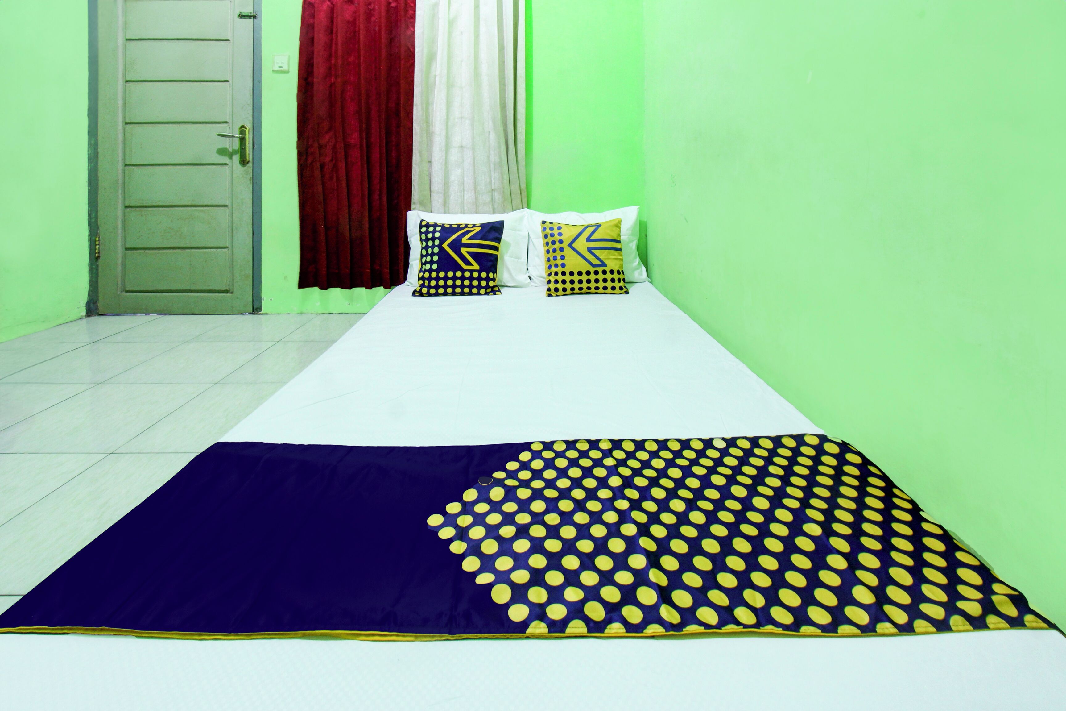 Una habitación con una cama, dos almohadas de diseños geométricos, una cortina roja y una pared verde.