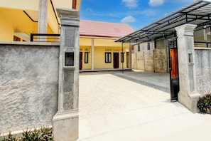 A courtyard with a yellow building, a covered area, and a tiled roof. - OYO Life 93255 Kosan Teratai Jaya (Janapria)