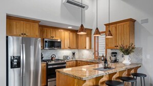 Una cocina moderna con armarios de madera, electrodomésticos de acero inoxidable y encimera de granito, además de taburetes de bar.