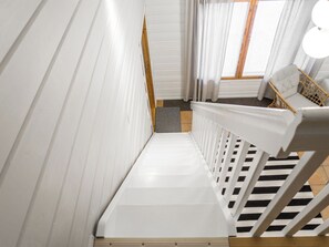 Un escalier avec des rampes blanches menant à une pièce où se trouve un fauteuil en osier et une fenêtre avec des rideaux.