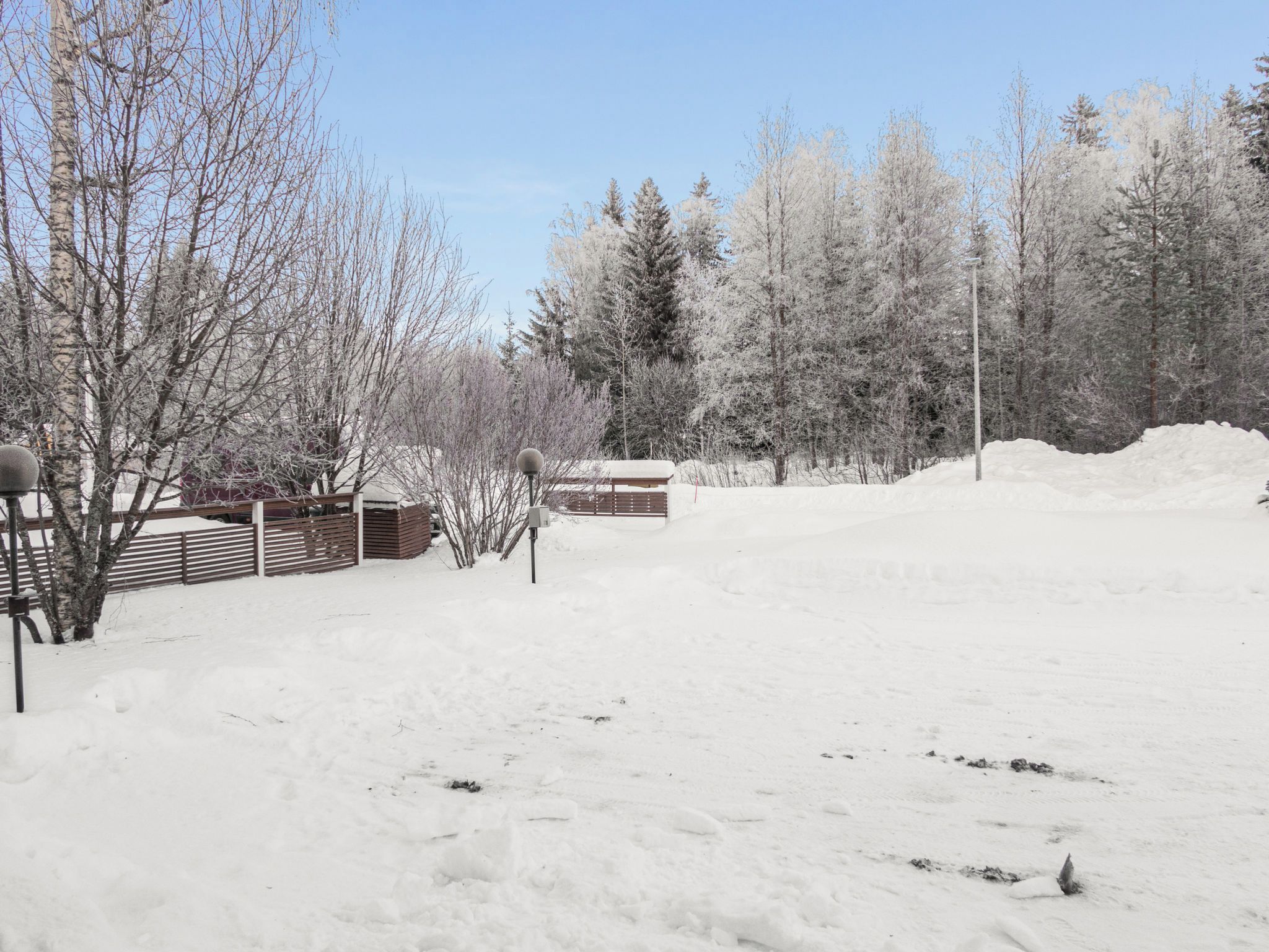 Un espacio exterior cubierto de nieve con una valla de madera, un banco y una colina nevada.