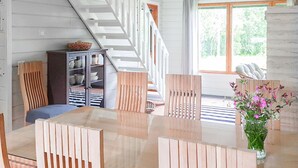 Un espace repas avec une table et des chaises en bois, un escalier et une vue sur la verdure à l’extérieur.